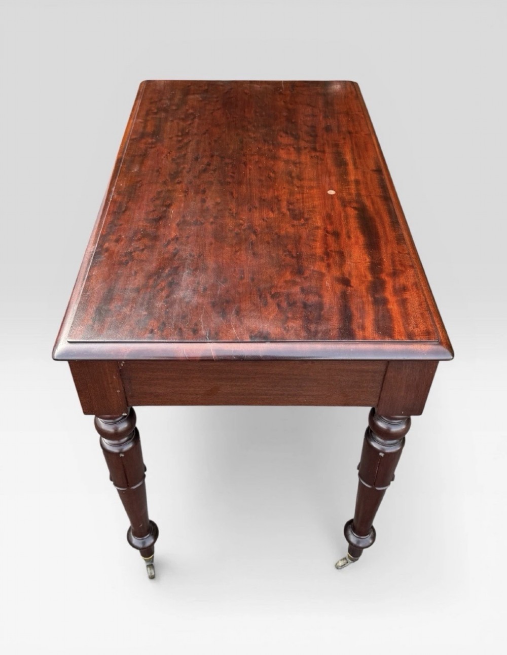 A Victorian dark mahogany side table featuring two drawers with circular wooden knobs, standing on four turned legs equipped with brass castors. View V