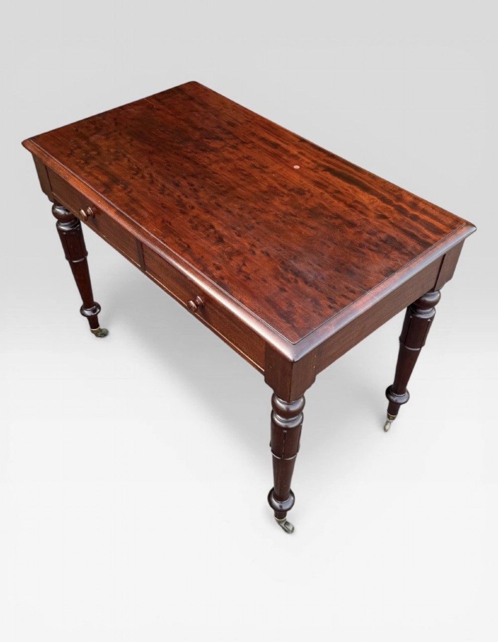 A Victorian dark mahogany side table featuring two drawers with circular wooden knobs, standing on four turned legs equipped with brass castors. View VI