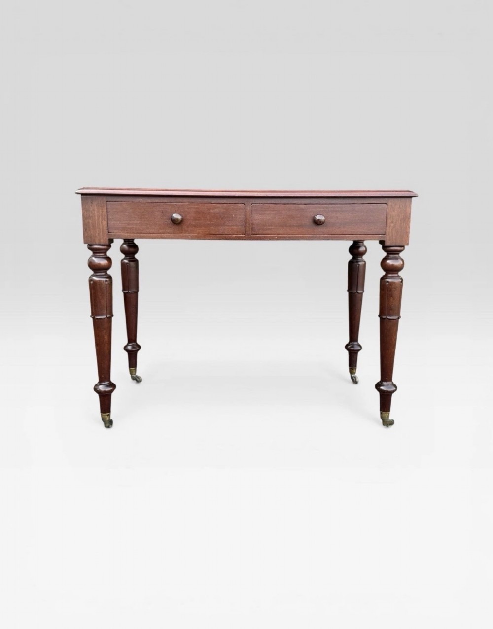 A Victorian dark mahogany side table featuring two drawers with circular wooden knobs, standing on four turned legs equipped with brass castors. View VIII