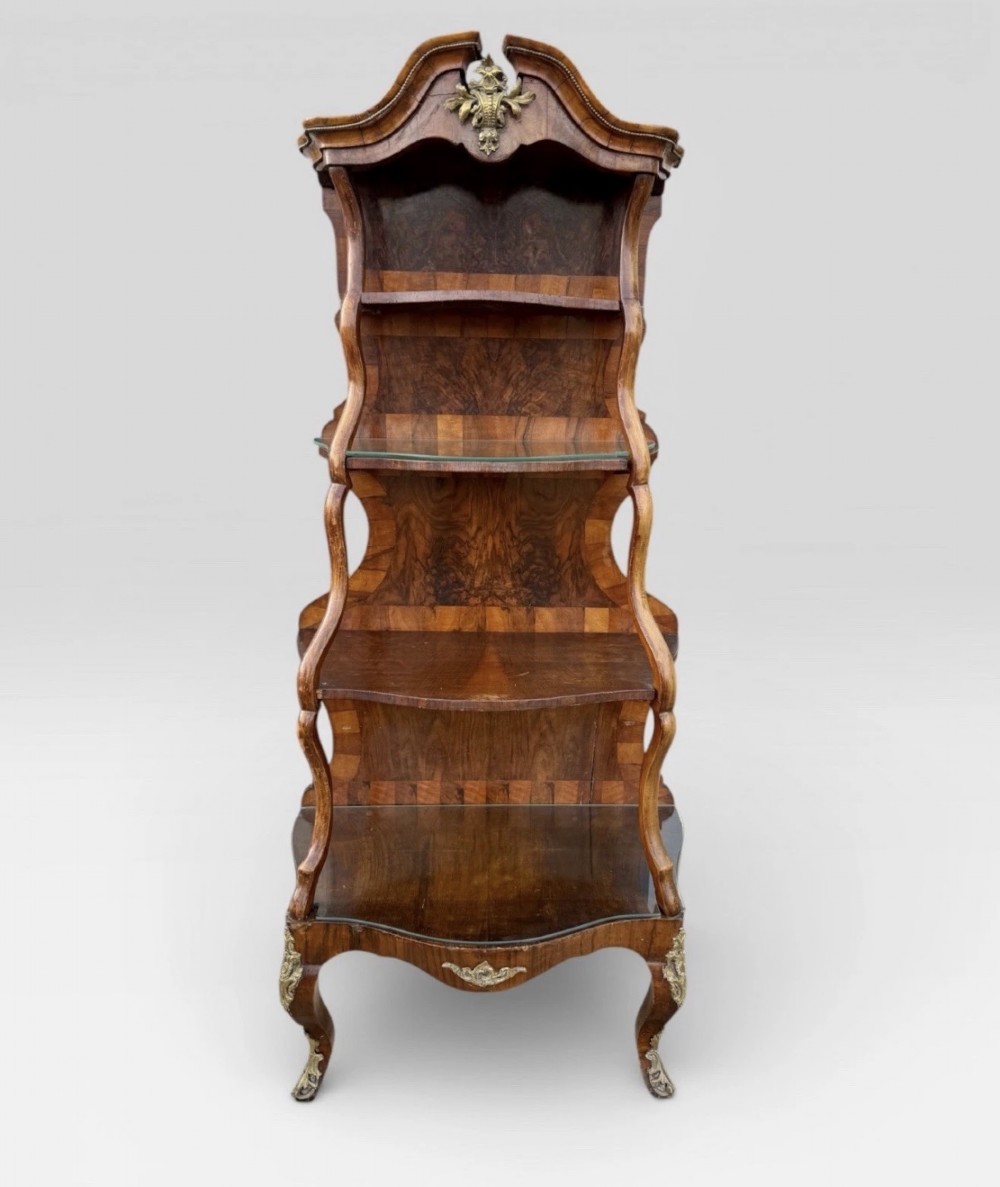 A nineteenth-century walnut etagere featuring open serpentine shelves, patterned wood veneers, ornate gilt metal mounts, and cabriole legs.
