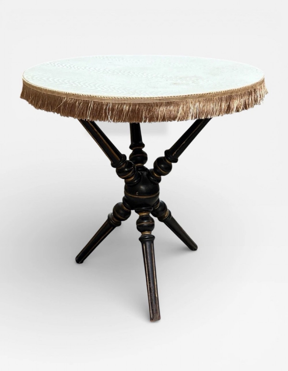 A Victorian Aesthetic Movement ebonised gypsy table with turned tripod legs, gilt highlights, and a cream fabric top with metallic fringe. View II