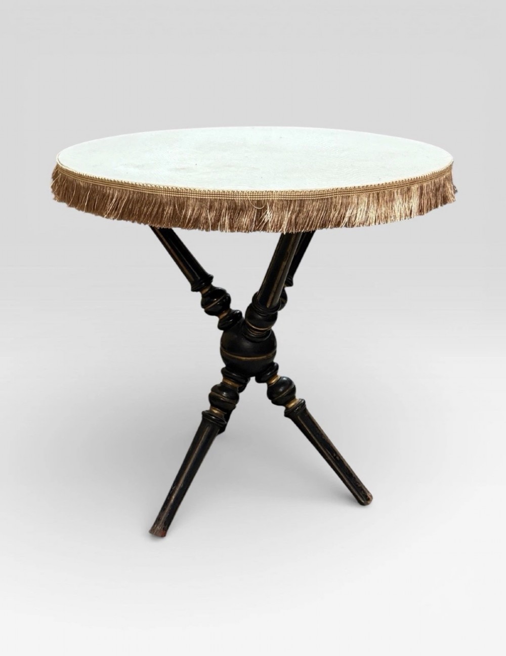 A Victorian Aesthetic Movement ebonised gypsy table with turned tripod legs, gilt highlights, and a cream fabric top with metallic fringe. View III