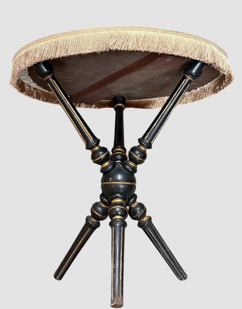 A Victorian Aesthetic Movement ebonised gypsy table with turned tripod legs, gilt highlights, and a cream fabric top with metallic fringe. View VII