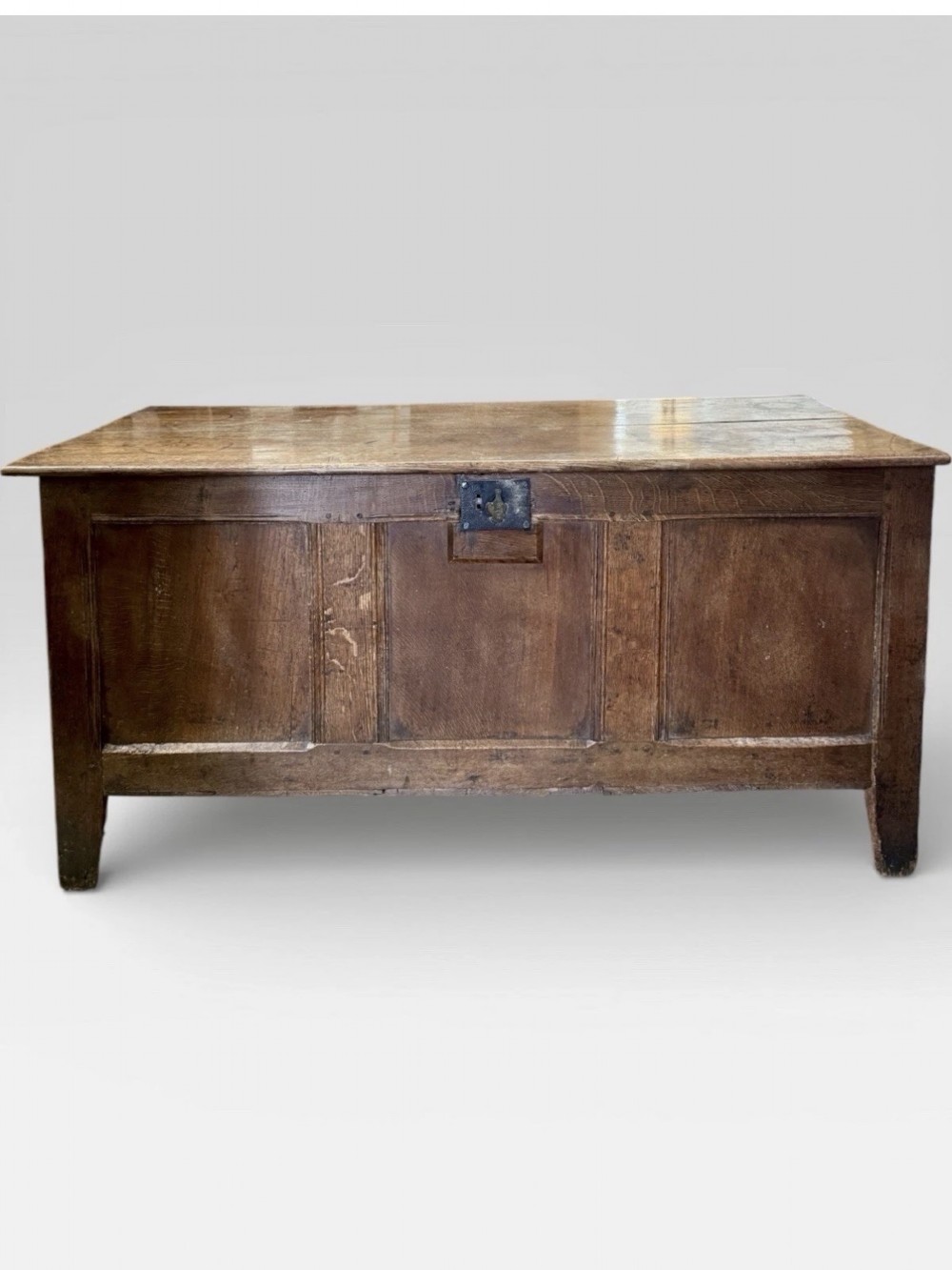 An antique 18th-century oak coffer featuring a three-panel front design and a central iron escutcheon lock plate.