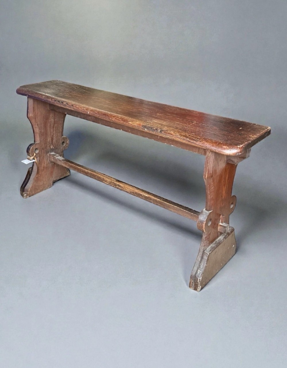 A dark warm brown antique pine organist bench with shaped side trestles and a low central connecting stretcher. View III