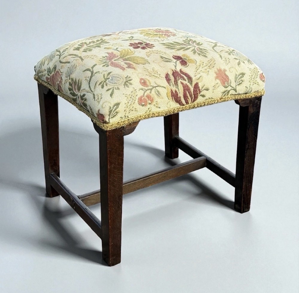 A square George III period wooden foot stool with straight dark timber legs, stretchers, and a cream floral tapestry upholstered padded top. View II