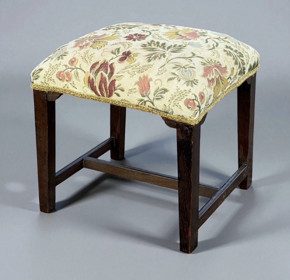 A square George III period wooden foot stool with straight dark timber legs, stretchers, and a cream floral tapestry upholstered padded top. View III