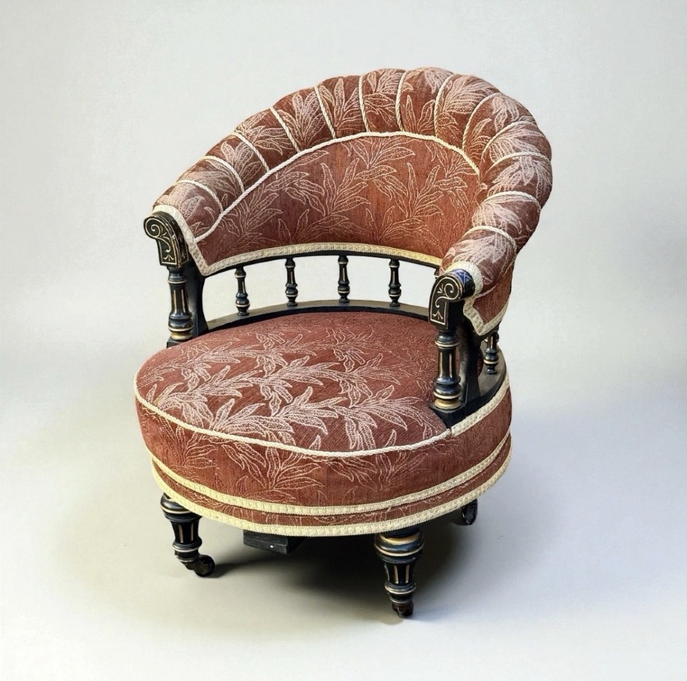 A Victorian ebonised revolving armchair upholstered in terracotta leaf-patterned fabric with turned gilt-accented spindles and castor feet.