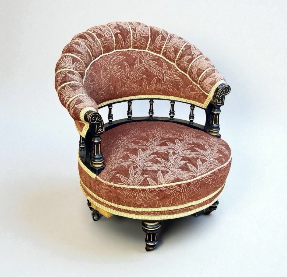 A Victorian ebonised revolving armchair upholstered in terracotta leaf-patterned fabric with turned gilt-accented spindles and castor feet. View II