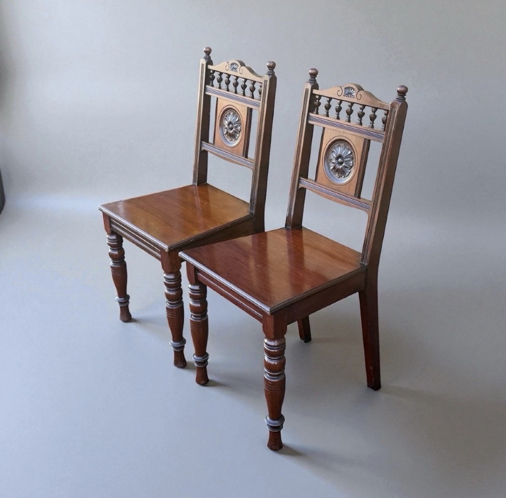 A pair of Victorian mahogany hall chairs featuring carved rosette back panels, spindled top rails, solid wood seats, and turned front legs. View III
