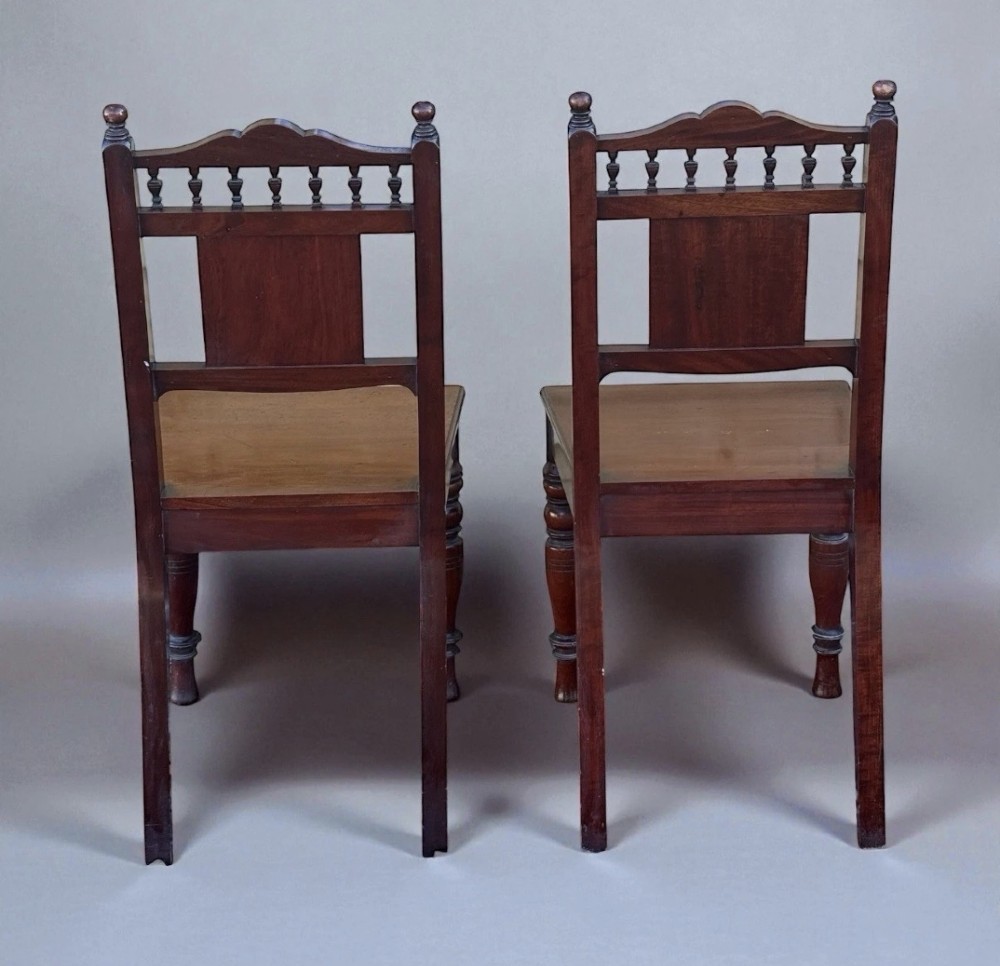 A pair of Victorian mahogany hall chairs featuring carved rosette back panels, spindled top rails, solid wood seats, and turned front legs. View IV
