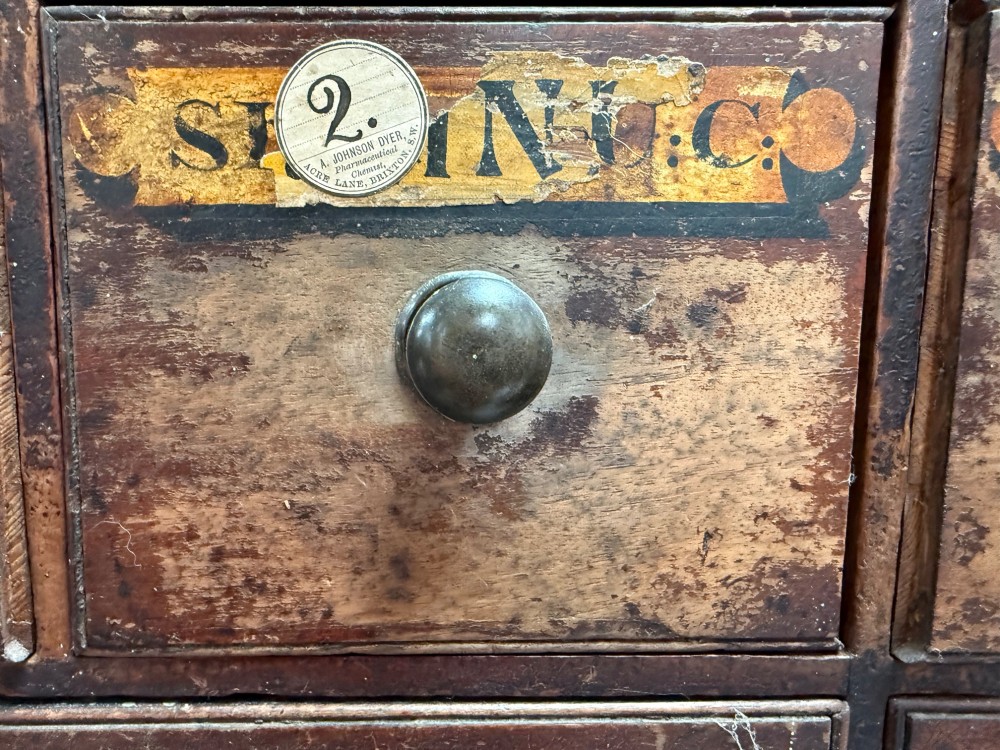 A 19th-century dark wood apothecary bank of drawers featuring twenty-six individual drawers with Latin botanical labels and turned knob handles. View IX