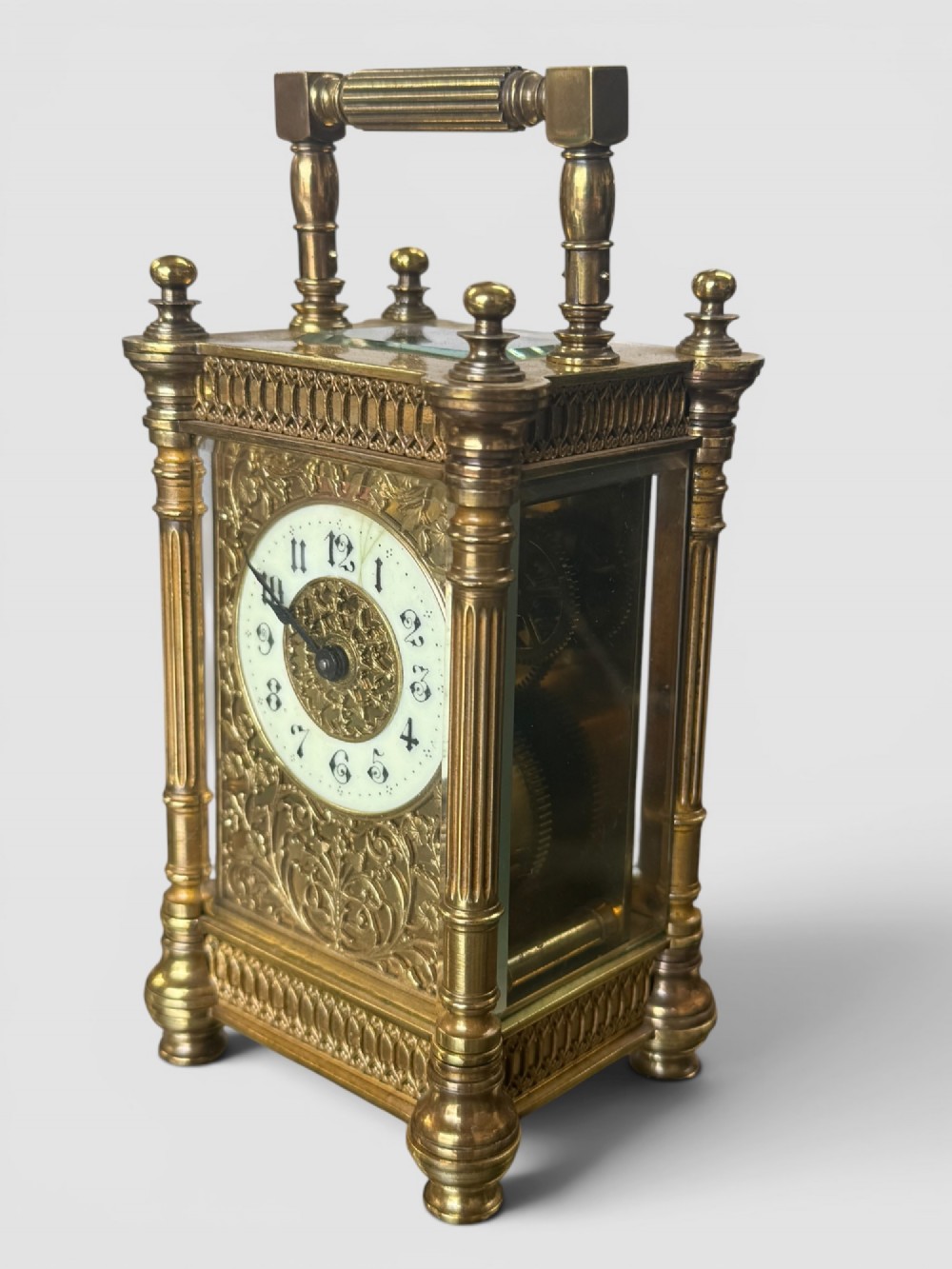 An ornate brass carriage clock featuring fluted corner columns, top finials, a carrying handle, and an engraved floral faceplate surrounding a circular enamel dial. View II