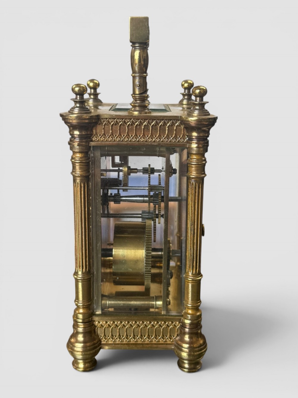 An ornate brass carriage clock featuring fluted corner columns, top finials, a carrying handle, and an engraved floral faceplate surrounding a circular enamel dial. View III