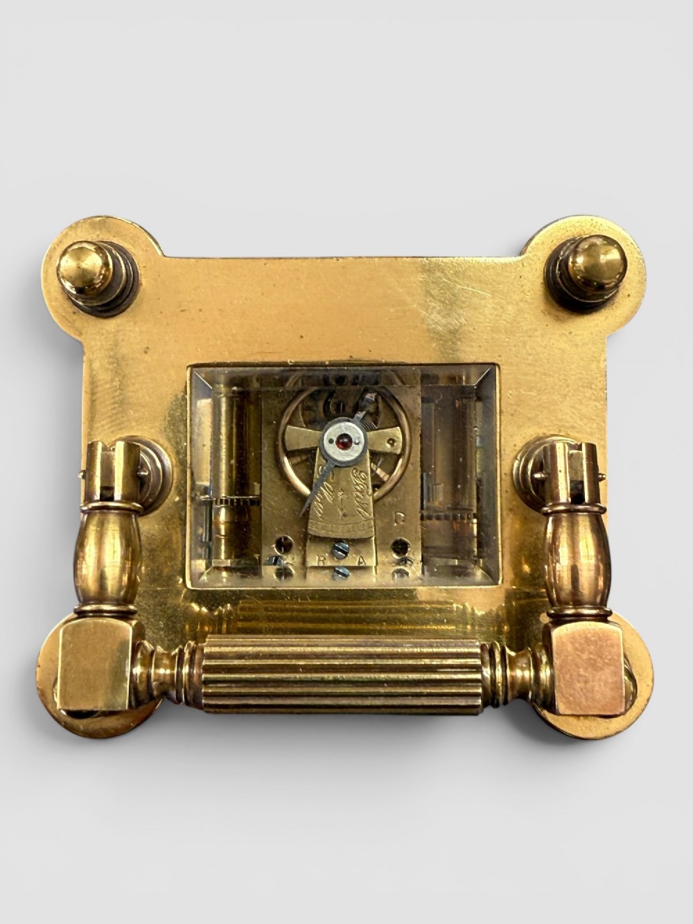 An ornate brass carriage clock featuring fluted corner columns, top finials, a carrying handle, and an engraved floral faceplate surrounding a circular enamel dial. View VII