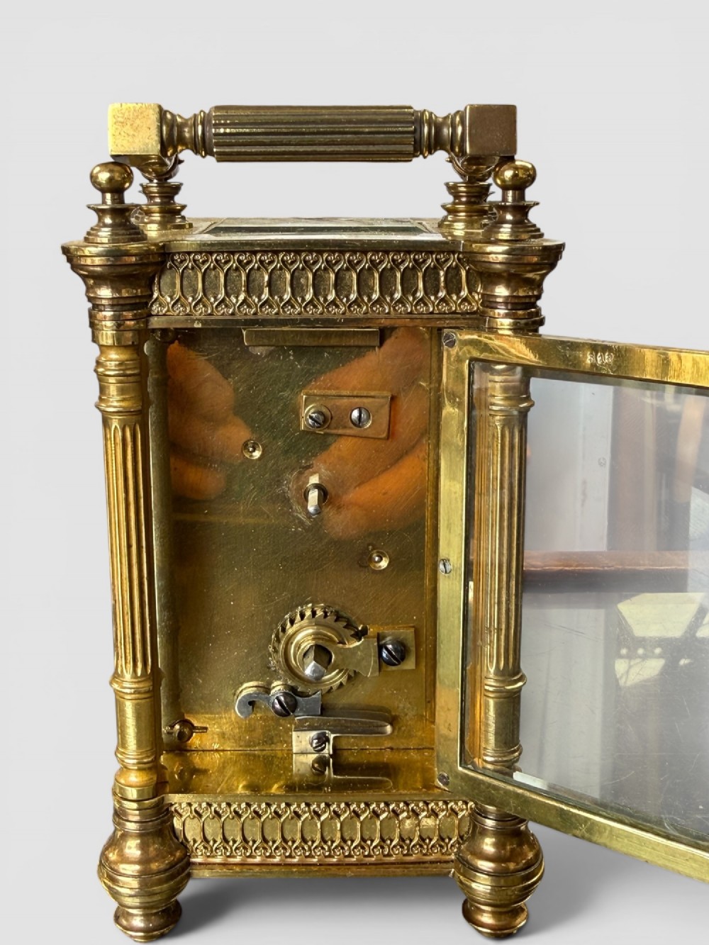 An ornate brass carriage clock featuring fluted corner columns, top finials, a carrying handle, and an engraved floral faceplate surrounding a circular enamel dial. View VIII