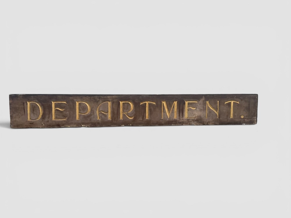 A long rectangular dark wooden sign with incised serif letters spelling DEPARTMENT gilded in gold leaf.