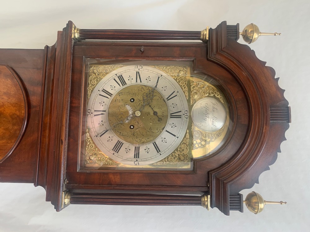 An antique Georgian longcase clock crafted from mahogany with brass finials, fluted trunk columns, and an arched brass dial. View II