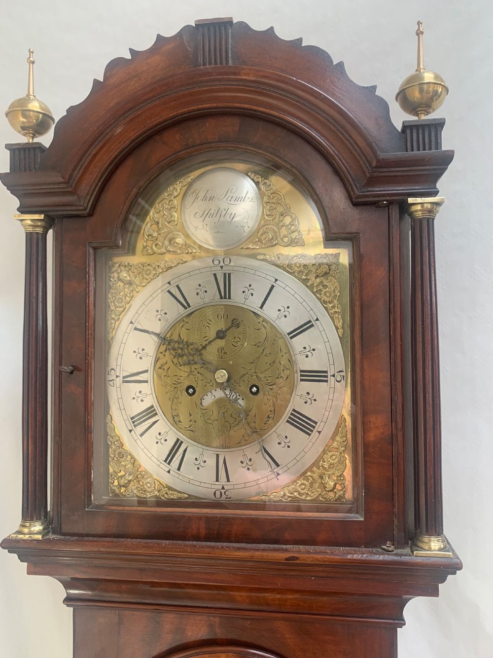 An antique Georgian longcase clock crafted from mahogany with brass finials, fluted trunk columns, and an arched brass dial. View III