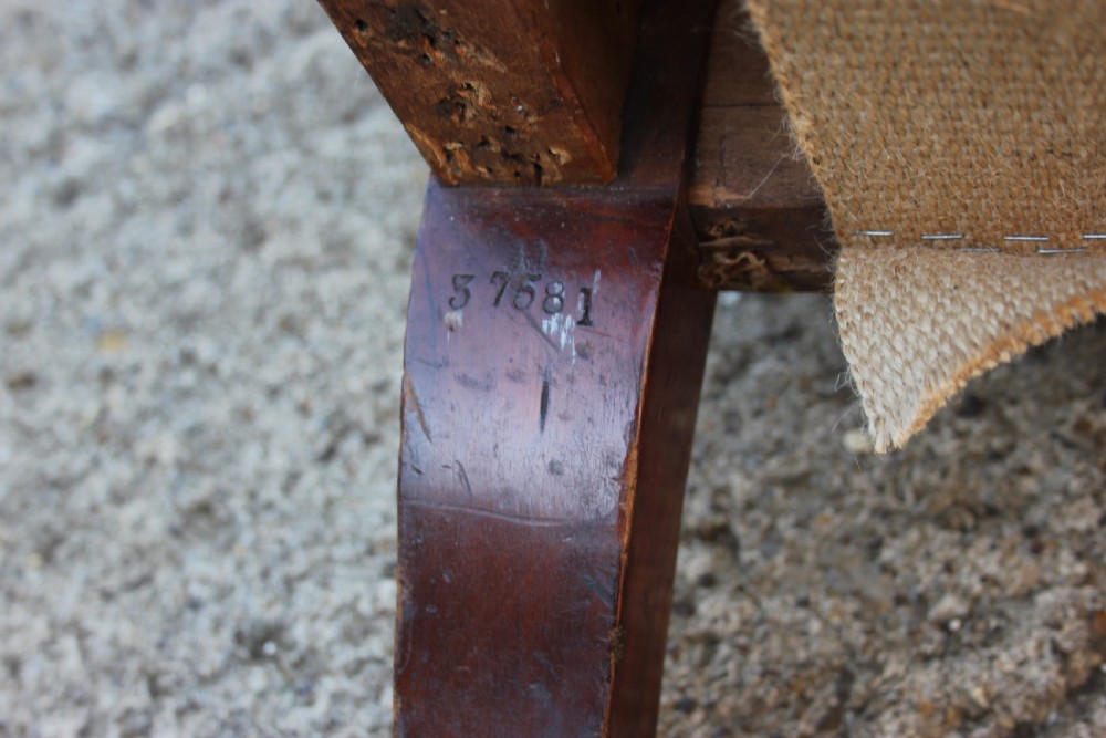 A Victorian armchair frame stripped to its base hessian upholstery, featuring turned mahogany front legs on brass castors. View V
