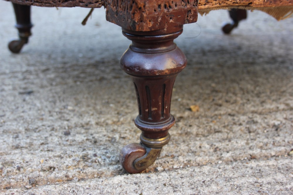 A Victorian armchair frame stripped to its base hessian upholstery, featuring turned mahogany front legs on brass castors. View VI