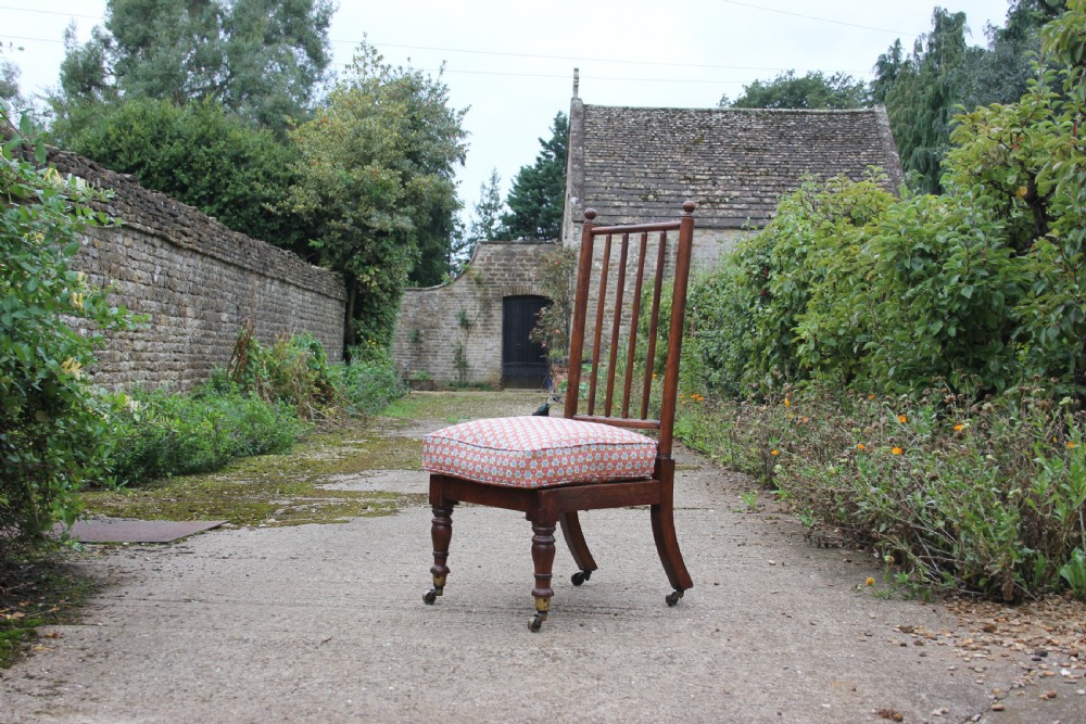 A 19th-century Victorian turned mahogany slipper chair with a spindle back and patterned upholstered seat resting on turned legs with brass castors.