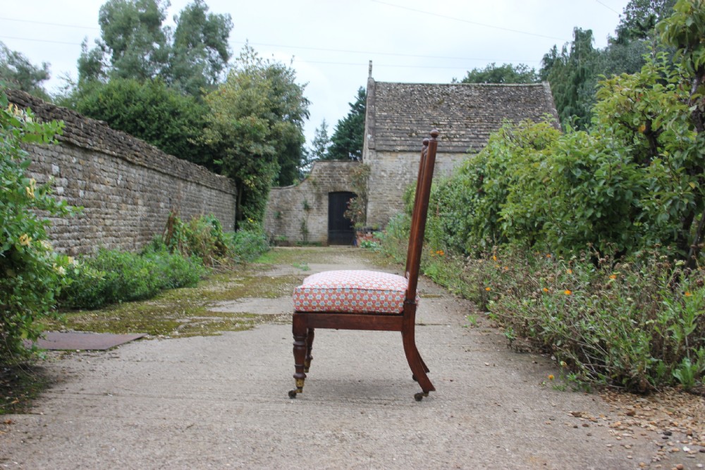 A 19th-century Victorian turned mahogany slipper chair with a spindle back and patterned upholstered seat resting on turned legs with brass castors. View II