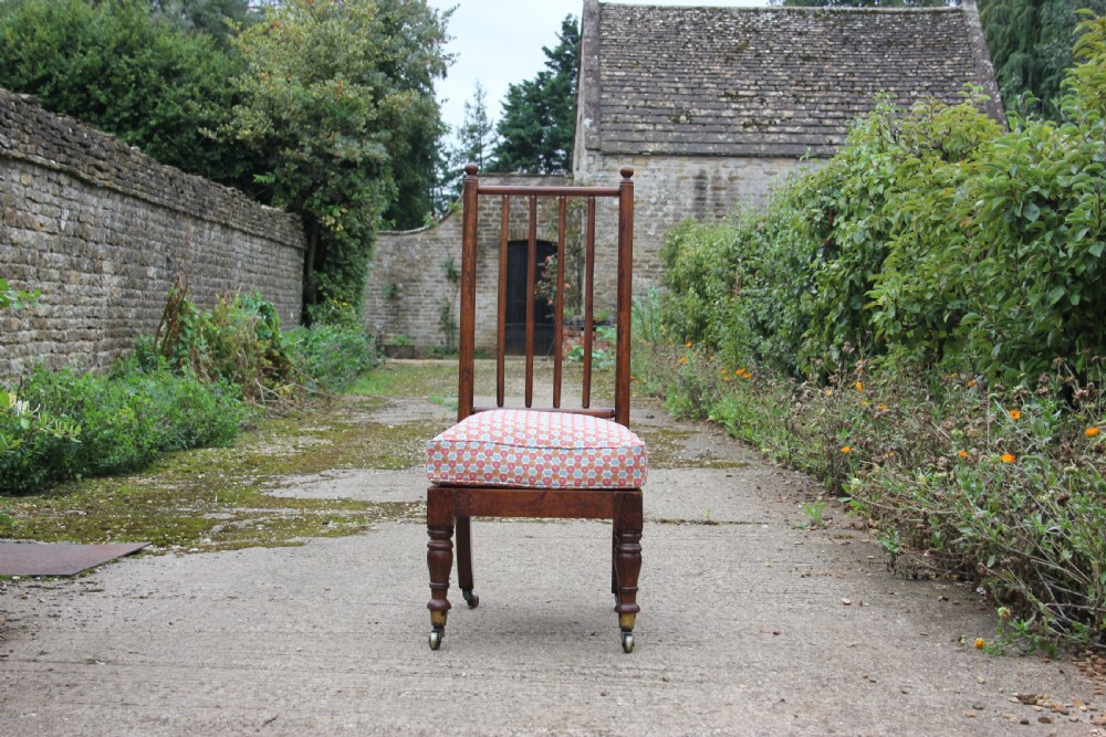 A 19th-century Victorian turned mahogany slipper chair with a spindle back and patterned upholstered seat resting on turned legs with brass castors. View V