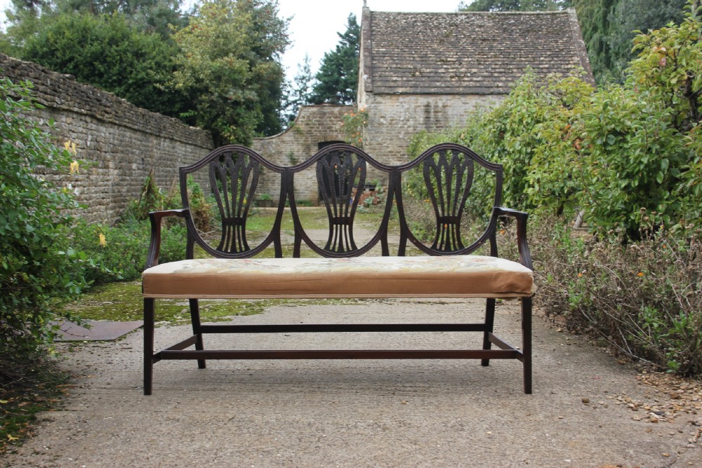A 19th century mahogany triple shield back settee with carved splats, curved arms, and an upholstered seat cushion. View II