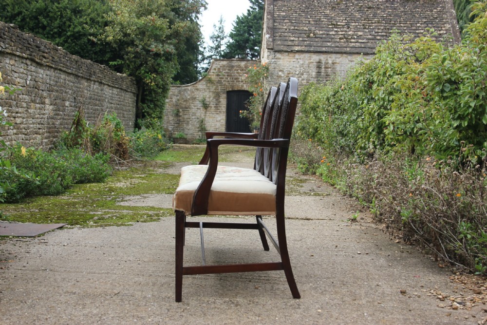 A 19th century mahogany triple shield back settee with carved splats, curved arms, and an upholstered seat cushion. View III