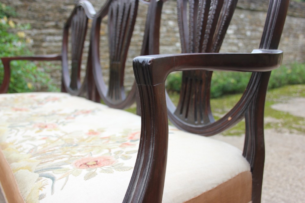 A 19th century mahogany triple shield back settee with carved splats, curved arms, and an upholstered seat cushion. View IV