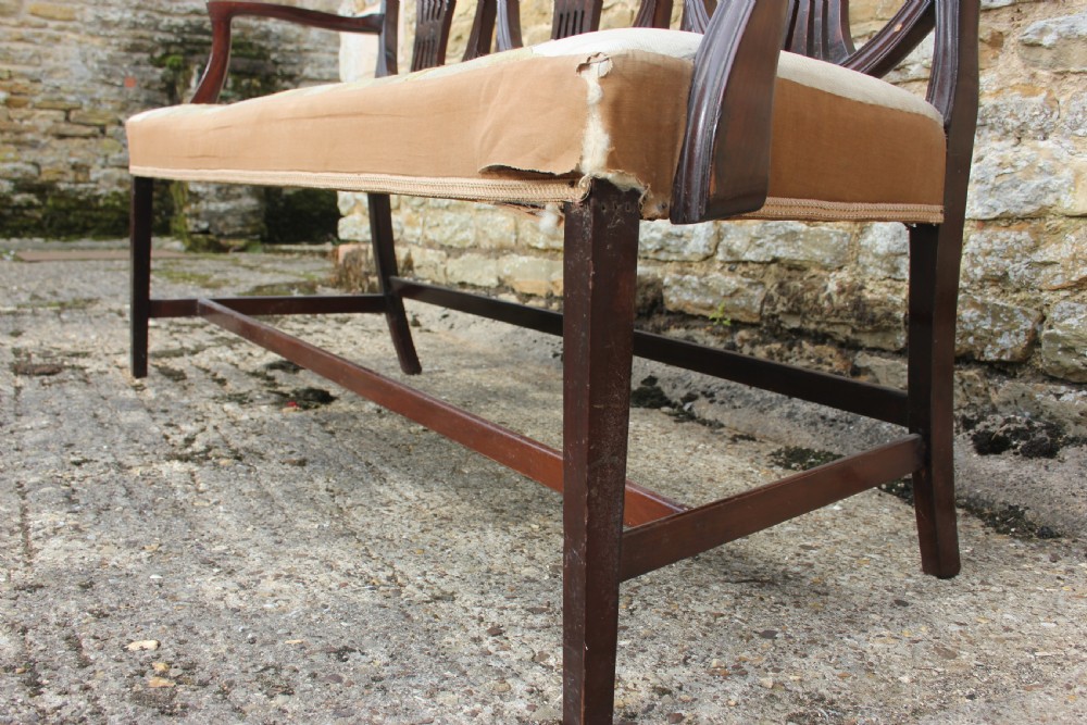 A 19th century mahogany triple shield back settee with carved splats, curved arms, and an upholstered seat cushion. View VI