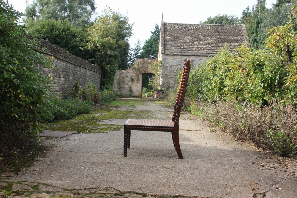 A 19th-century dark rosewood side chair featuring lathe-turned bobbin legs and backrest spindles with a woven cane seat. View II