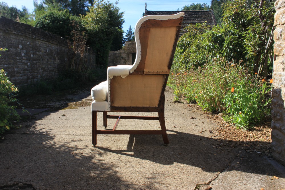 An 18th-century wingback armchair upholstered in off-white calico lining with dark mahogany legs, an H-stretcher frame, and brass castors. View II