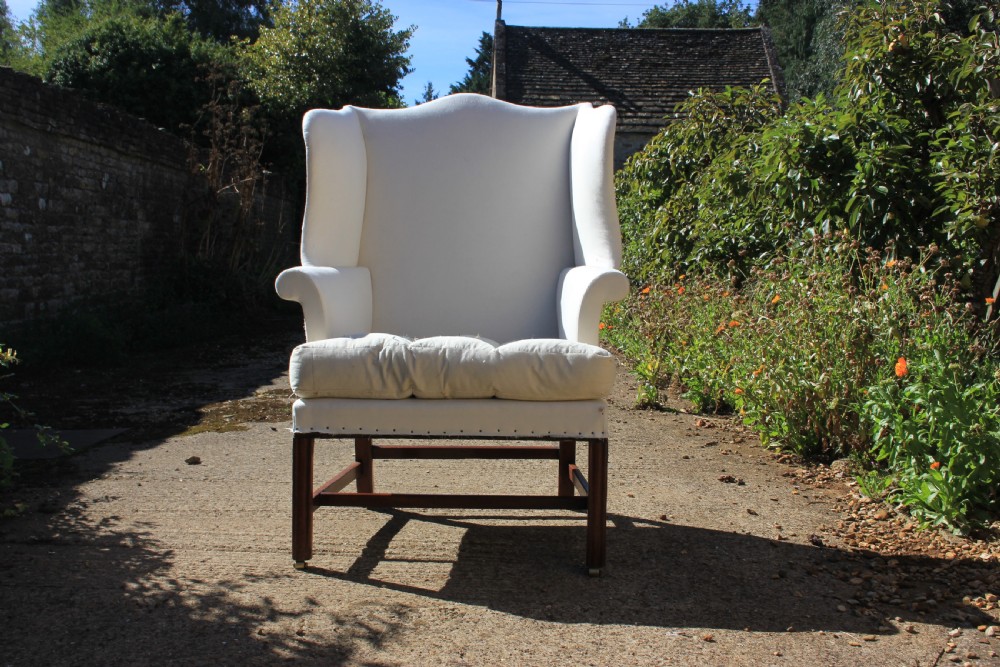 An 18th-century wingback armchair upholstered in off-white calico lining with dark mahogany legs, an H-stretcher frame, and brass castors. View III