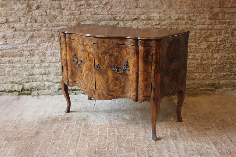 An eighteenth-century Italian walnut commode featuring a serpentine curved front, two panel doors, cabriole legs, and dark metal handles.