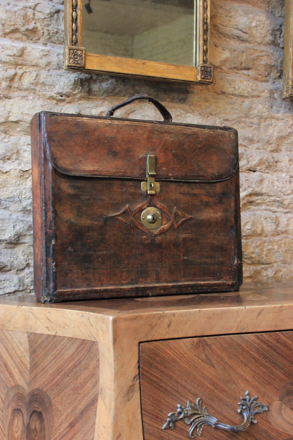 A 19th-century patinated brown leather attache case featuring a top handle, fold-over flap, brass clasp, and decorative embossed detailing around a central brass keyhole.