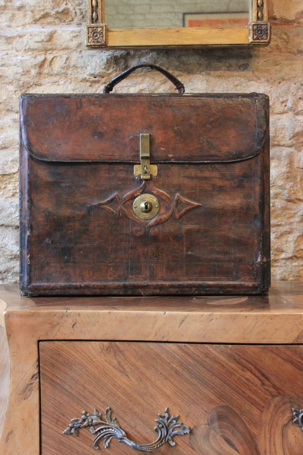 A 19th-century patinated brown leather attache case featuring a top handle, fold-over flap, brass clasp, and decorative embossed detailing around a central brass keyhole. View III