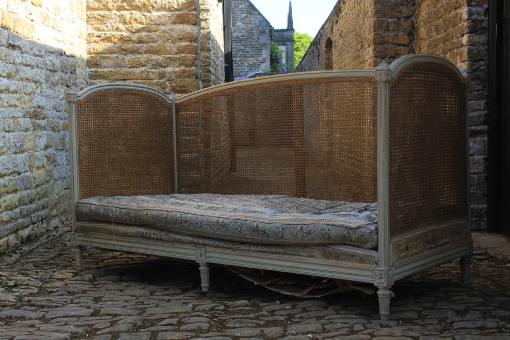 A French Louis XVI style painted wood daybed sofa featuring hand-woven cane panels along the arched back and sides, resting on fluted tapered legs with an upholstered cushion.