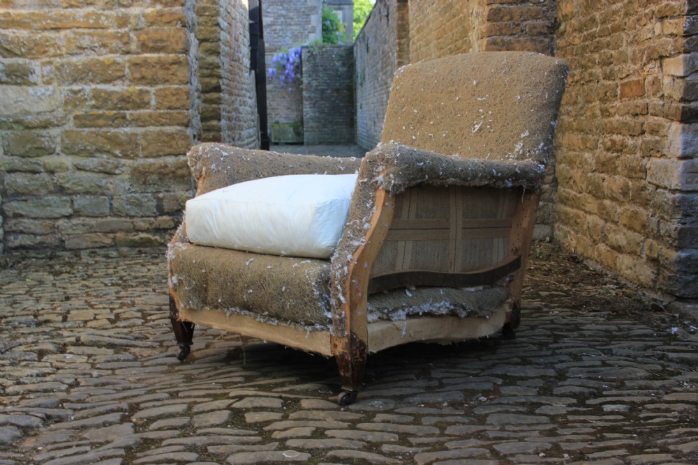 A Howard style armchair frame prepared for re-upholstery with turned front legs on castors, exposed hessian structure, and a white cushion base.