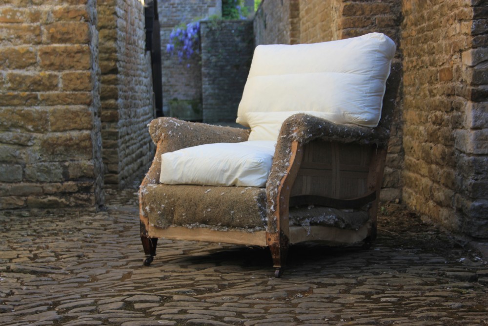 A Howard style armchair frame prepared for re-upholstery with turned front legs on castors, exposed hessian structure, and a white cushion base. View II