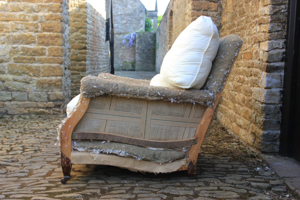 A Howard style armchair frame prepared for re-upholstery with turned front legs on castors, exposed hessian structure, and a white cushion base. View III