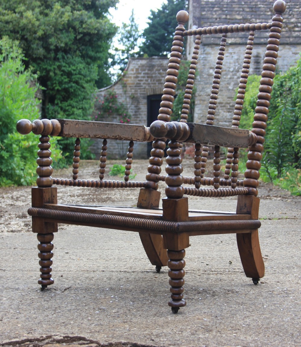 A 19th-century walnut armchair frame featuring lathe-turned bobbin spindles on the backrest, legs, and arm supports on small brass castors.