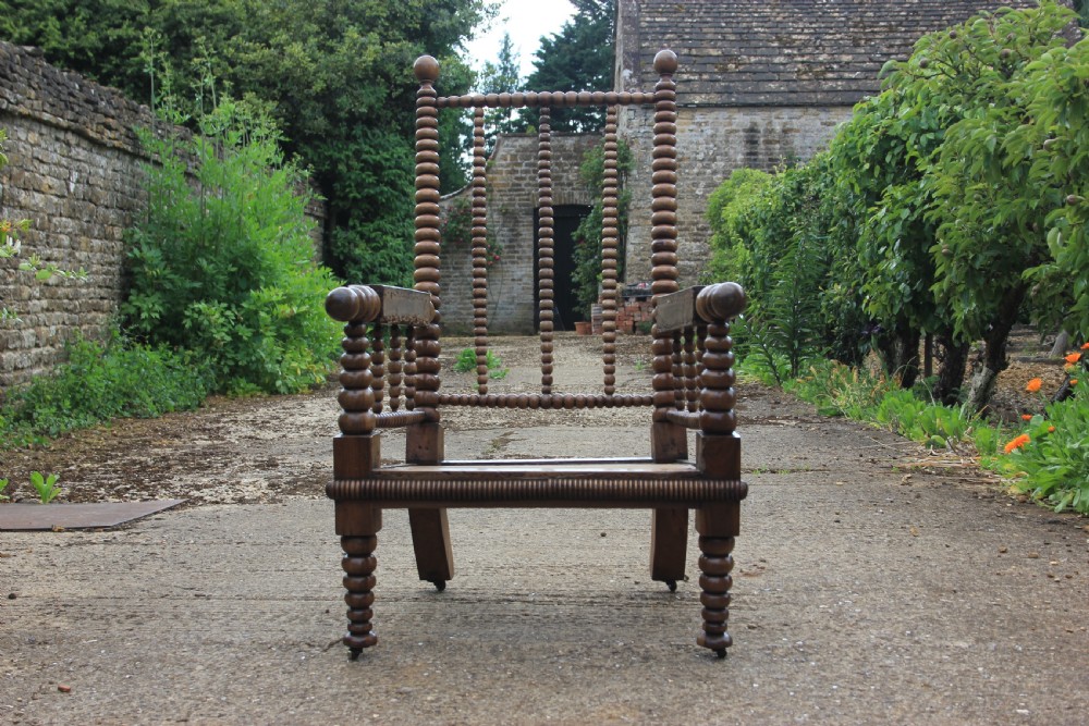 A 19th-century walnut armchair frame featuring lathe-turned bobbin spindles on the backrest, legs, and arm supports on small brass castors. View II