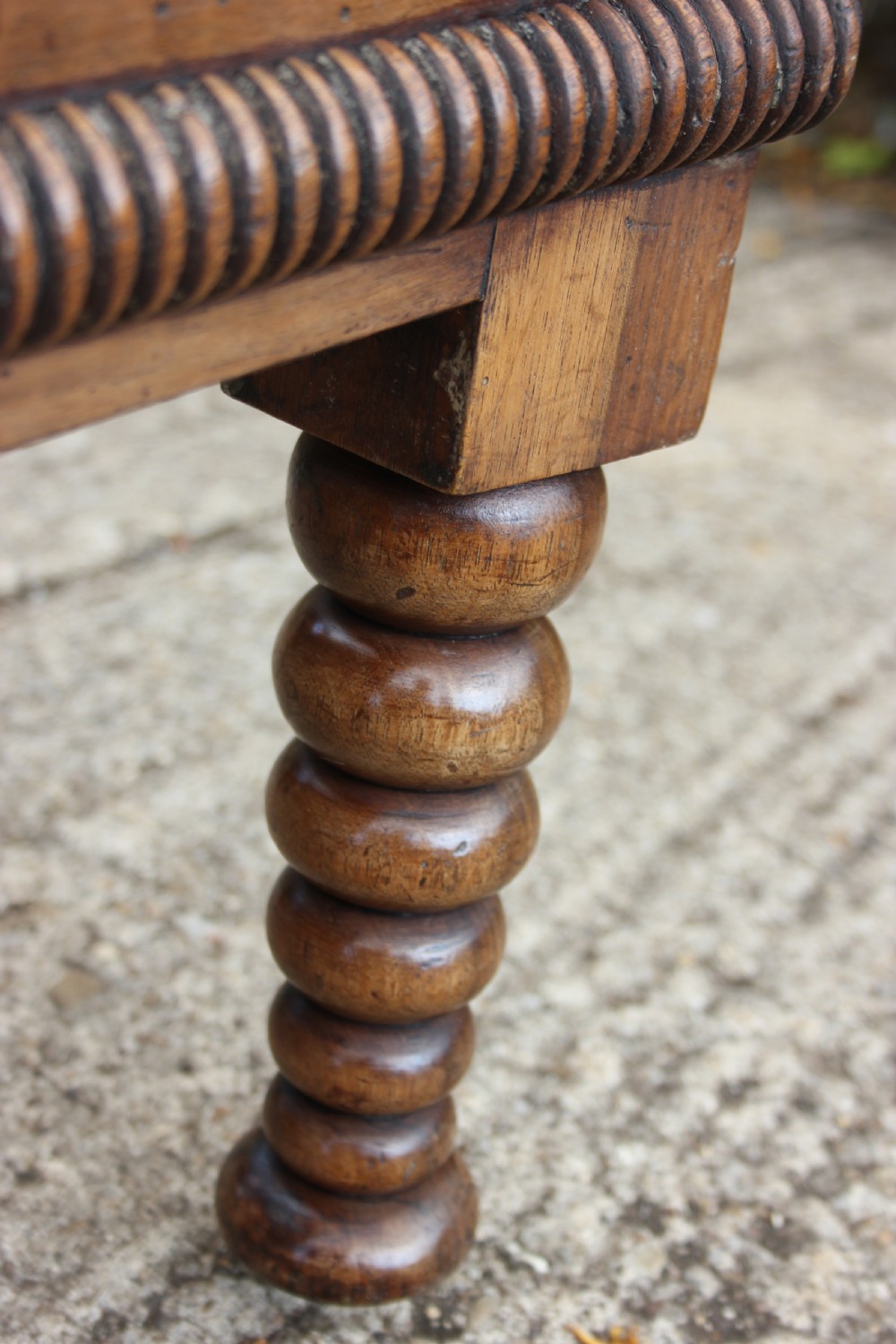 A 19th-century walnut armchair frame featuring lathe-turned bobbin spindles on the backrest, legs, and arm supports on small brass castors. View VII