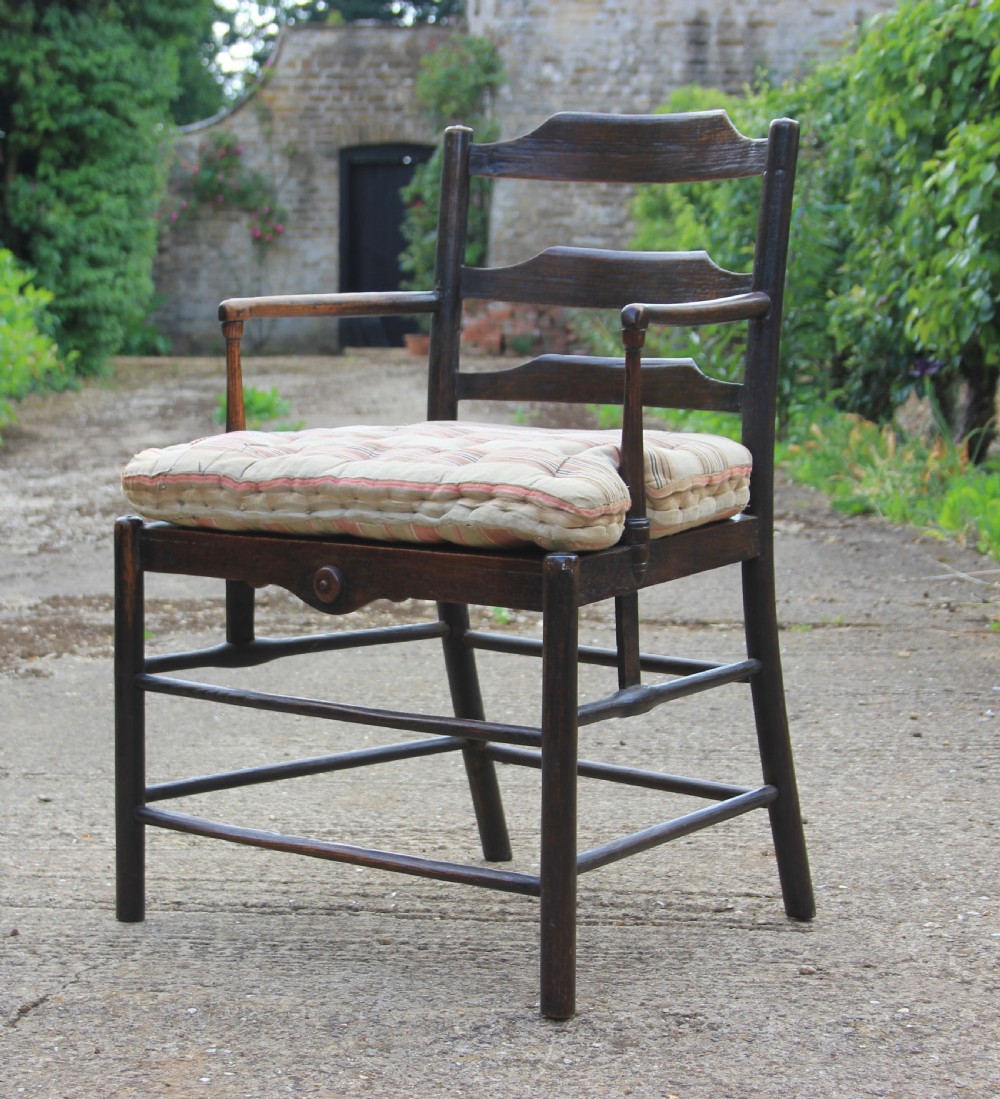An 18th-century dark ash Sussex armchair featuring turned uprights, a ladderback frame, shaped armrests, and a striped fabric seat cushion.