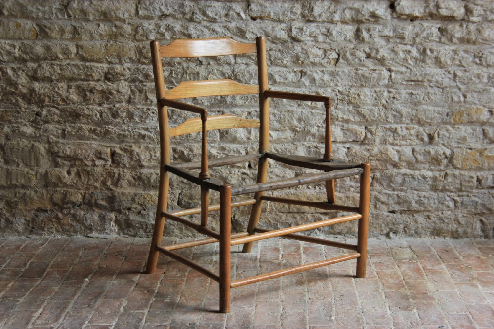 A low-slung Scandinavian light wood nursing chair featuring horizontal ladderback splats, turned arm supports, and multiple stretchers.
