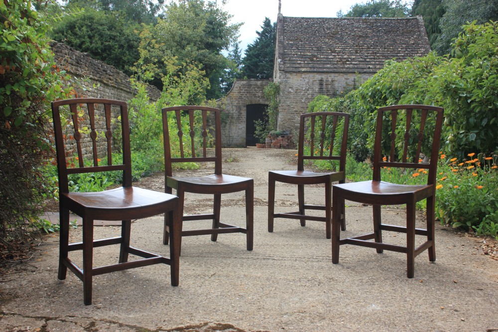 A set of four dark wood antique dining chairs with vertical spindle backs and contoured wooden seats.
