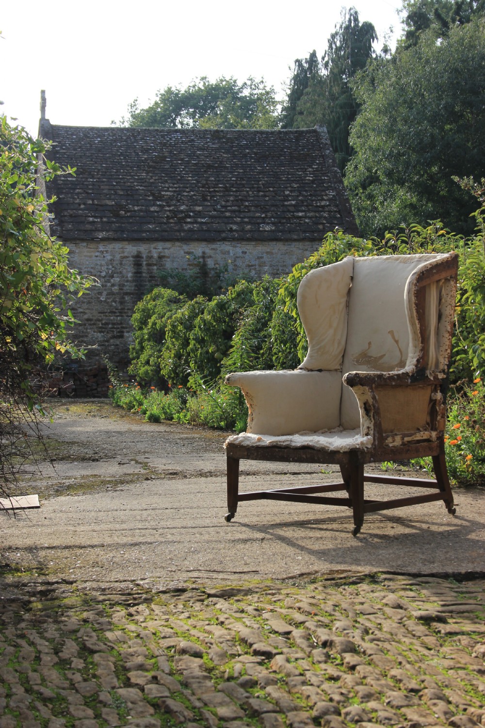 An early 18th-century wingback armchair featuring a dark timber frame, prominent side wings, and worn beige calico upholstery.