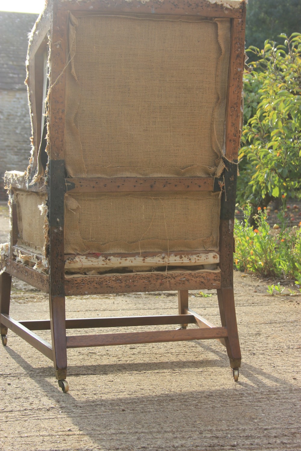 An early 18th-century wingback armchair featuring a dark timber frame, prominent side wings, and worn beige calico upholstery. View III